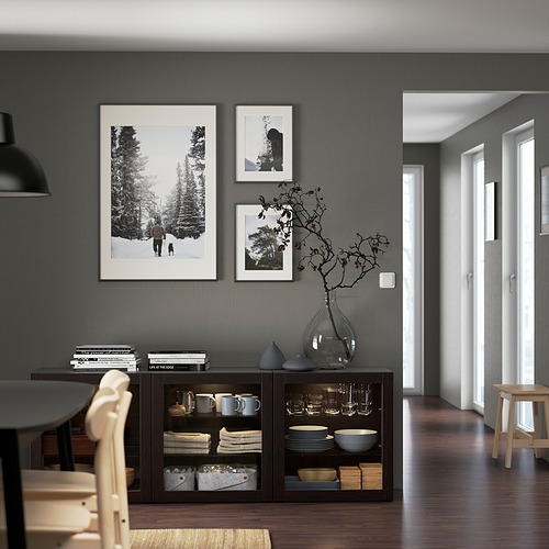Comedor gris oscuro con pantalla BESTÅ, fotos en blanco y negro y jarrón de vidrio. Pasillo de madera clara.