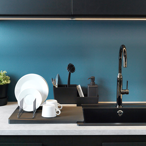Fregadero de cocina moderno con un secadero de platos que sostiene platos y tazas blancas. Un dispensador de jabón y un cepillo para fregar están cerca, contra un salpicadero azul.