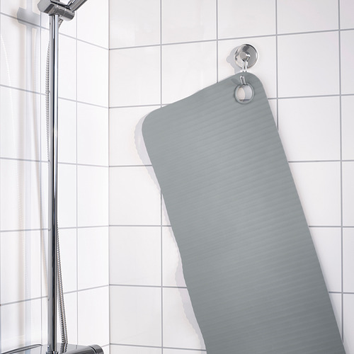 La alfombra de baño gris cuelga del gancho de pared en la ducha con azulejos, asegurada por ventosas.