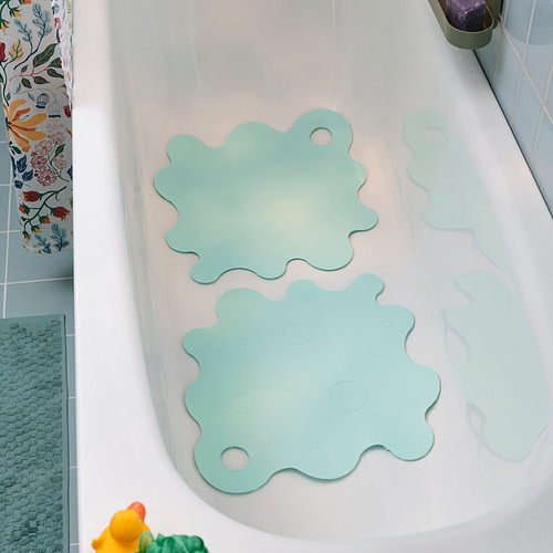 Dos alfombras de baño TRAMPSJÖN de color turquesa claro con ventosas en una bañera blanca junto a una cortina de ducha de colores.