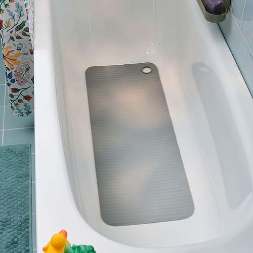 Una bañera blanca con una alfombra de textura azul, una alfombra gris antideslizante y una cortina de ducha floral.