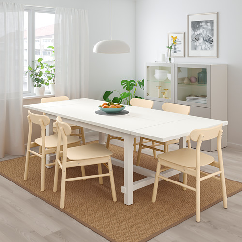 Mesa de comedor extensible de madera blanca con 6 sillas, centro de mesa sobre alfombra.