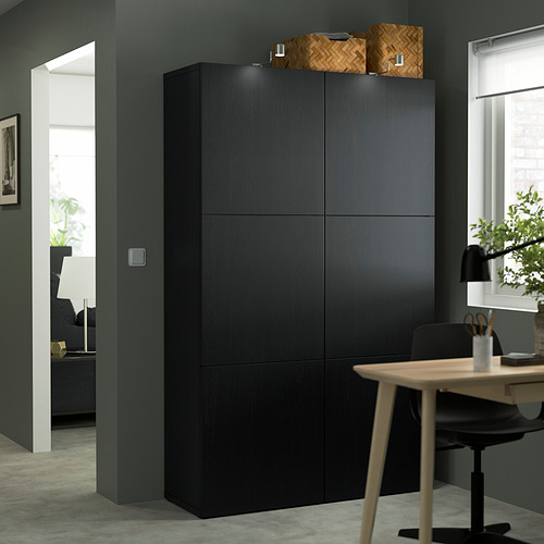 This image shows a tall, black BESTÅ storage unit, larger than a nearby desk, with woven baskets on top.