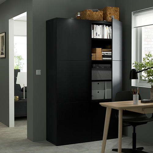 Modern home office setup with black BESTÅ storage cabinet featuring adjustable shelves, books, and a wooden desk with a chair.