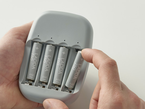 Hand inserting a LADDA rechargeable battery into a gray battery charger.