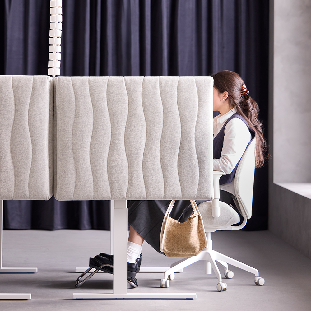 Office scene with a person sitting at a workspace separated by a beige MITTZON acoustic screen in Gunnared beige.