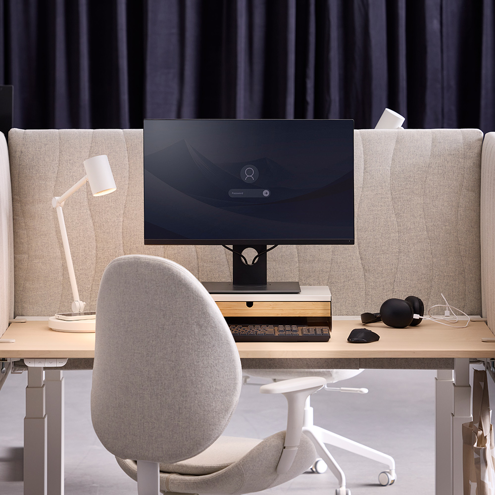 A desk setup with a beige MITTZON acoustic screen made from Gunnared fabric that separates two workspaces from each other.