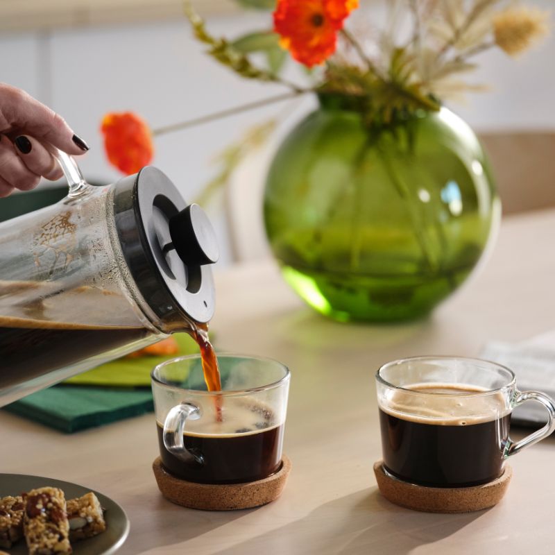 Minimal coffee table scene with IKEA 365+ cup and coasters, UPPHETTA coffee maker, MOSSMAL dessert plate and cereal bar.