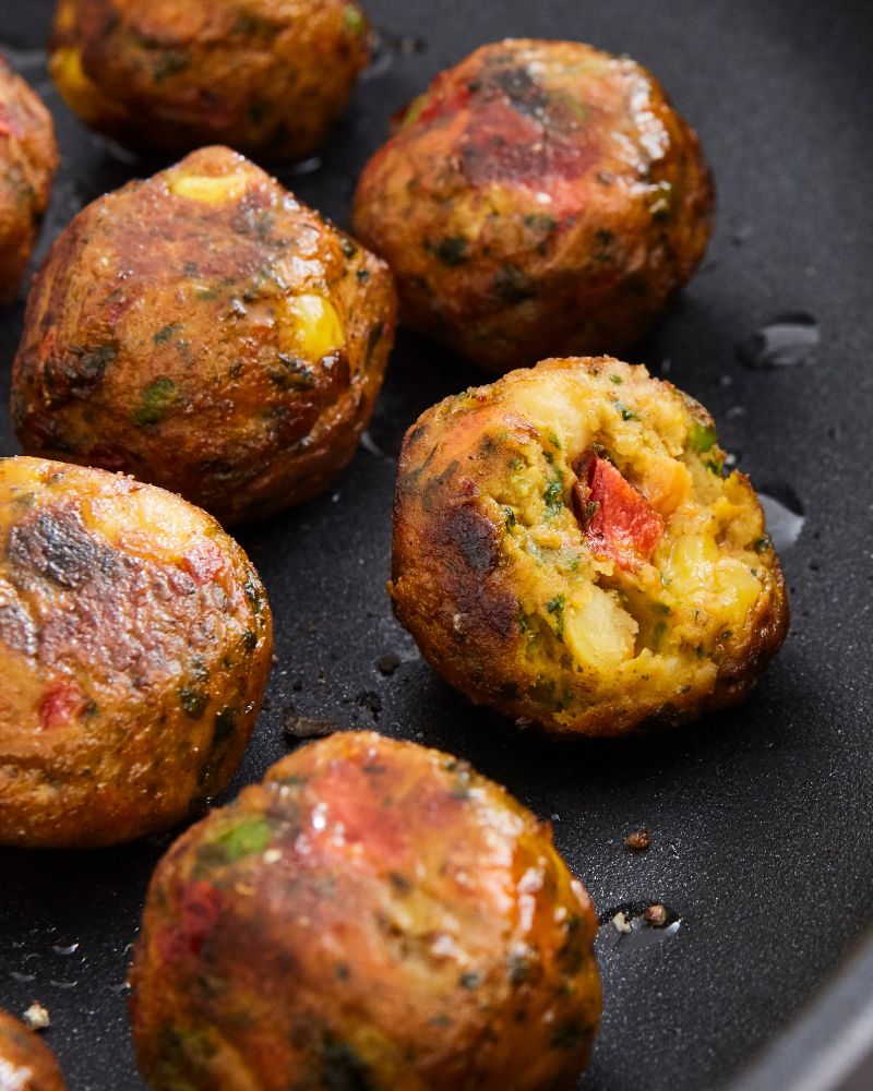 Hot pan close-up with rustic style featuring HEMLAGAD frying pan and HUVUDROLL vegetable balls, golden and ready to serve.