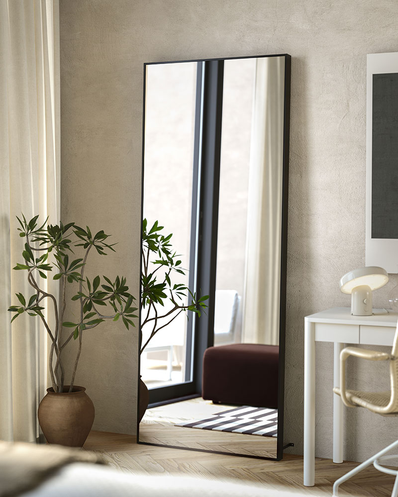 A full-length black HOVET mirror stands on the oor, against an o-white bedroom wall, reecting bright natural light.