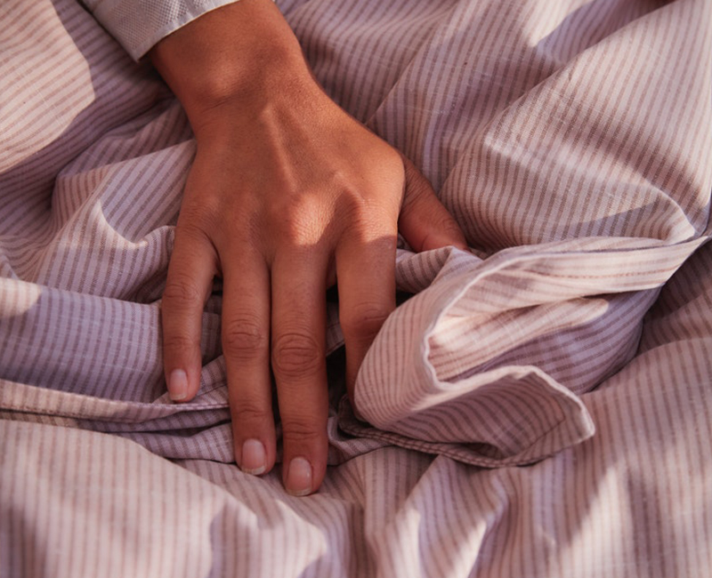 Hand on light pink striped textile, likely IKEA BERGPALM bedding. Soft feel.
