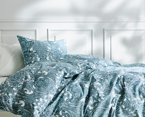 Una cama con una funda nórdica azul y blanca de cachemir y una almohada blanca.