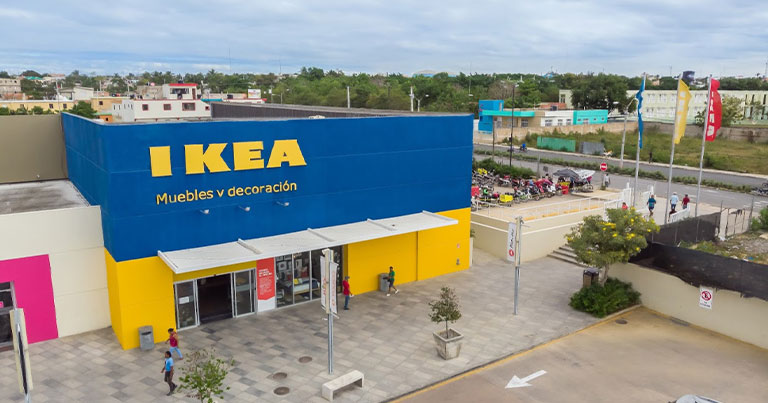 Main entrance of a blue and yellow IKEA store with people walking on the pavement.