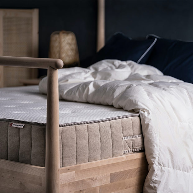 Shot of a corner of a pine style bed, with the mattress visible and a fluffy white comforter on top.