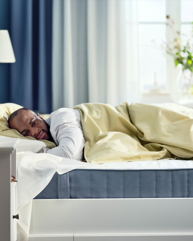 A person comfortably sleeping on a modern style bed, the blue mattress is visible, in the background the blue and white curtain is out of focus.