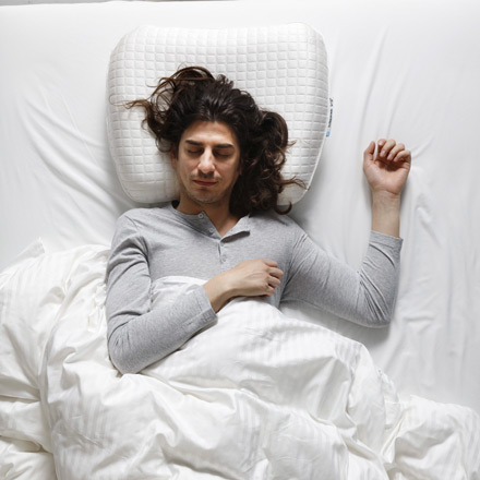 Person lying face up, on white comforters and with an orthopedic pillow.