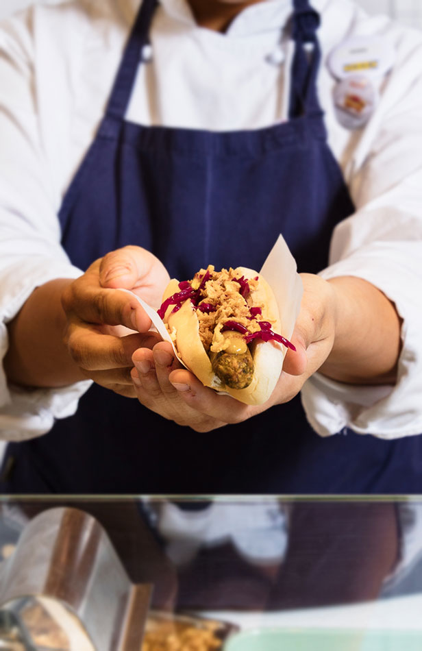 Chef holding a veggie hot dog toward the camera, showcasing a tasty and sustainable meat-free option.