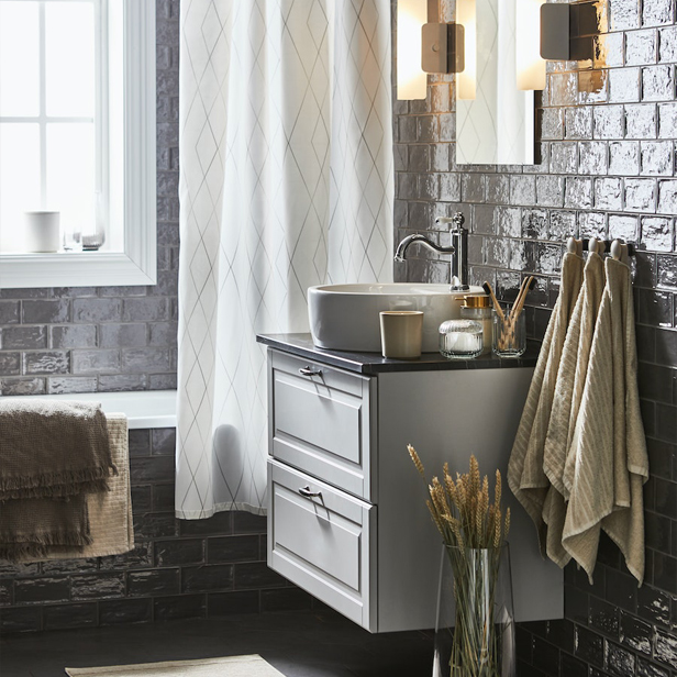 A bathroom with a cabinet featuring a TÄNNFORSEN/TÖRNVIKEN washbasin, VÅGSJÖN bath towels, and a HAVSDUN LED wall lamp."