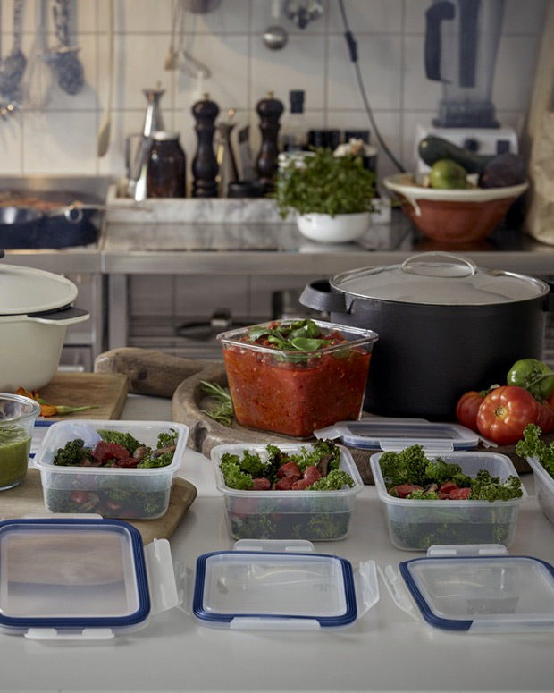 Meal prep scene: containers with salads and sauce on a kitchen counter with pots and fresh produce.