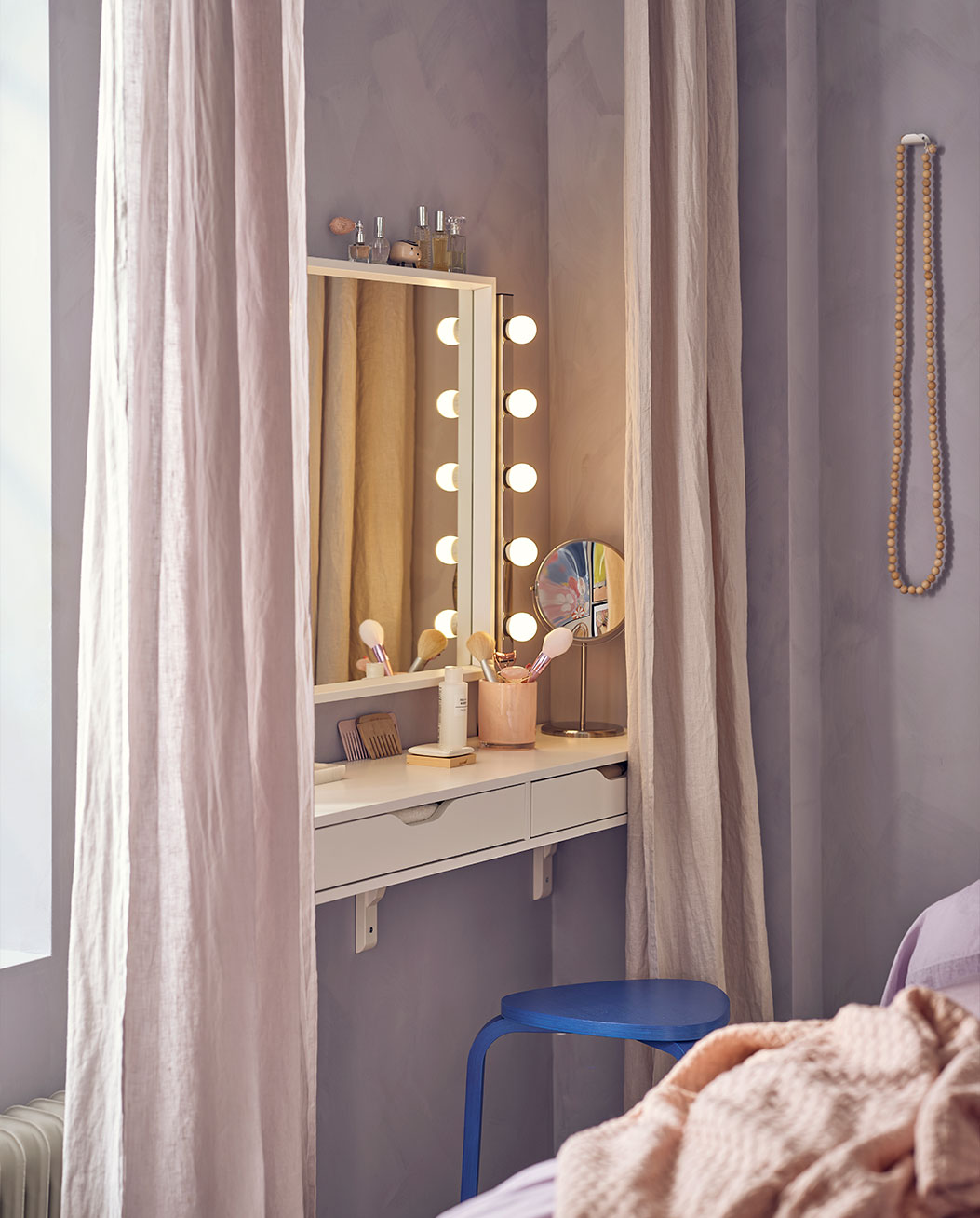 Mirror surrounded by lights next to a shelf console with soft curtains
