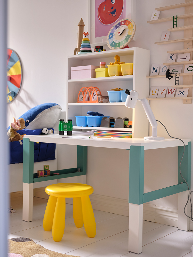 A PÅHL children's desk with GLIS boxes with lids on top, also a KRUX LED lamp and a yellow MAMMUT stool.