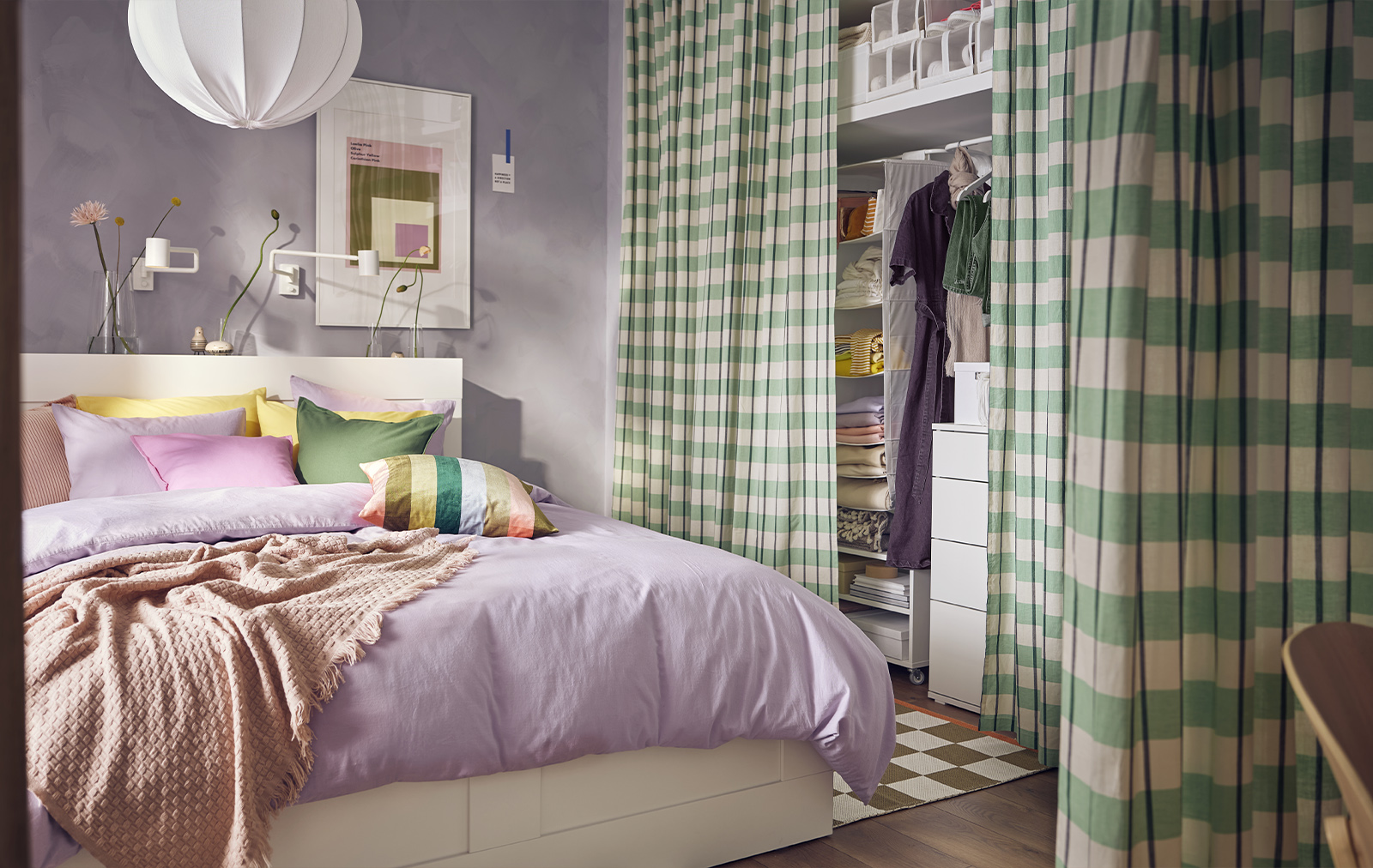 Colorful bedroom, a large bed with brightly colored cushions, a light purple cover and a closet with green plaid colors.