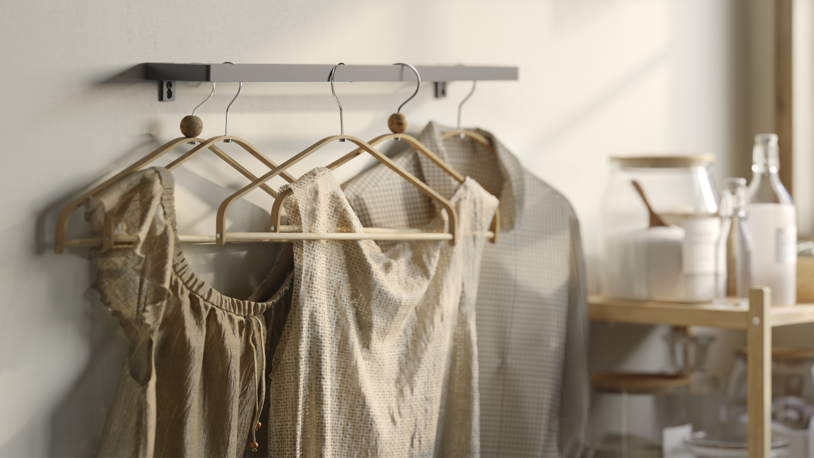 Neutral-toned clothing hanging on HÖSVANS bamboo hangers beneath a wall-mounted rail.