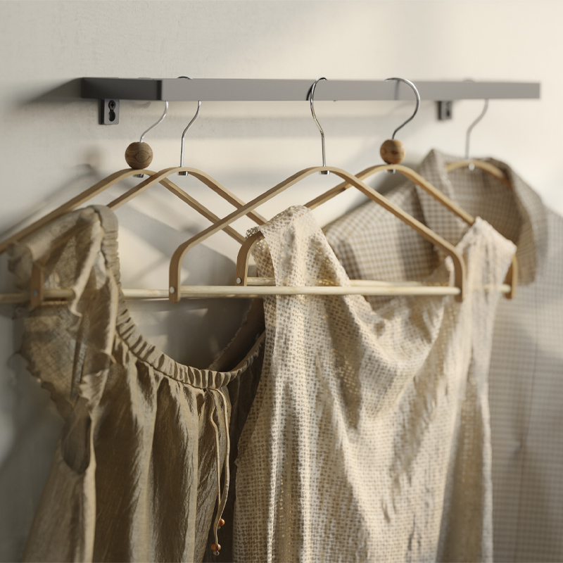 Neutral-toned clothing hanging on HÖSVANS bamboo hangers beneath a wall-mounted rail.