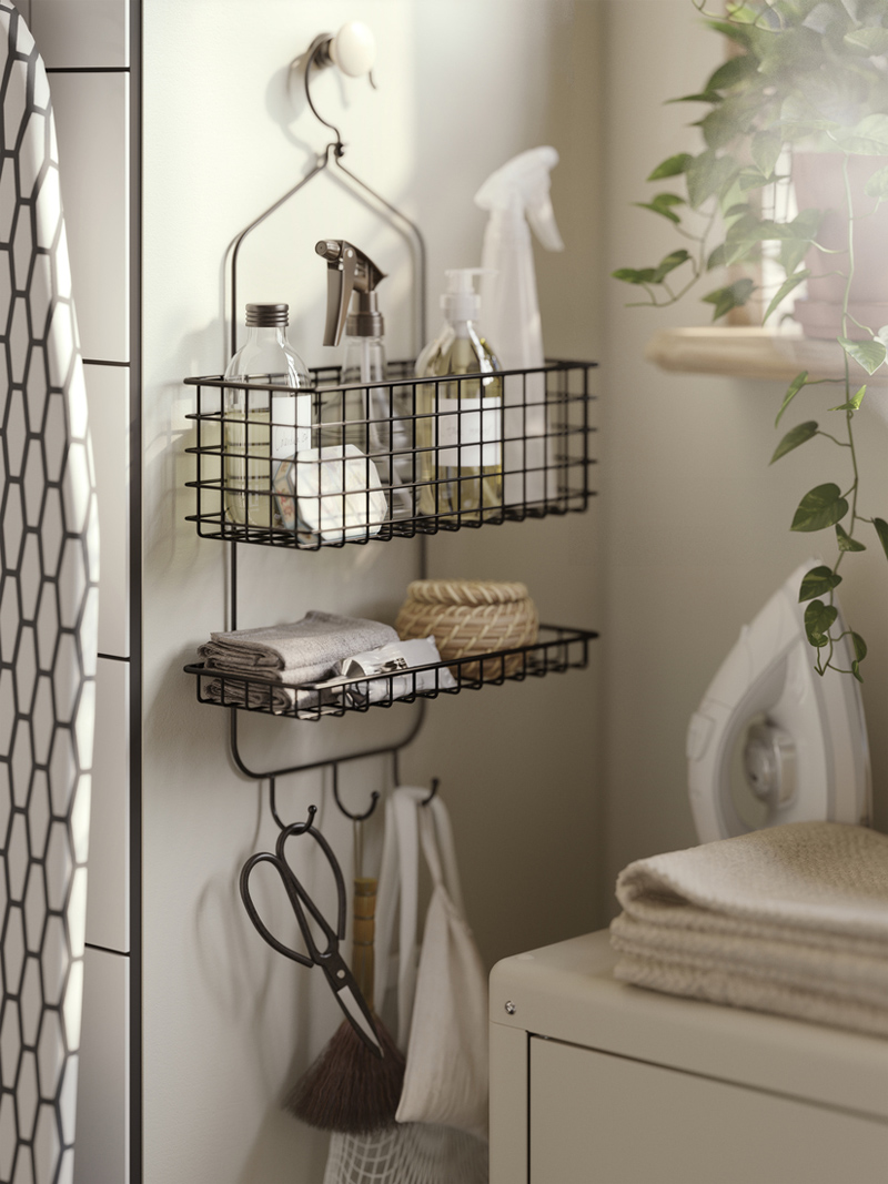 BLECKSJÖN black wire wall organizer holding cleaning bottles, towels, and basket in soft light
