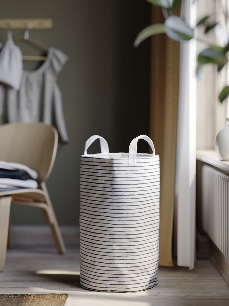 KLUNKA striped laundry bag in a bright corner with wooden furnishings and soft daylight.