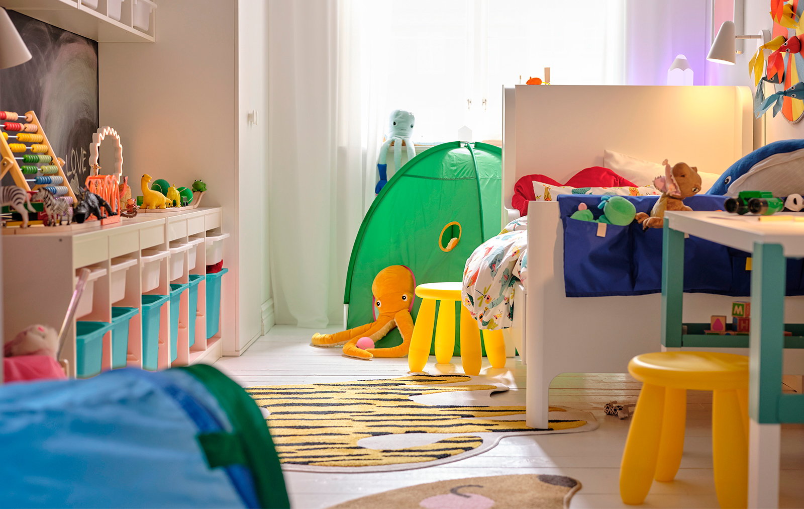 A children's room with a TROFAST storage system on the left, a PAHL desk on the right with two yellow MAMMUT stools, and a DVÄRGMÅS tent in the background.