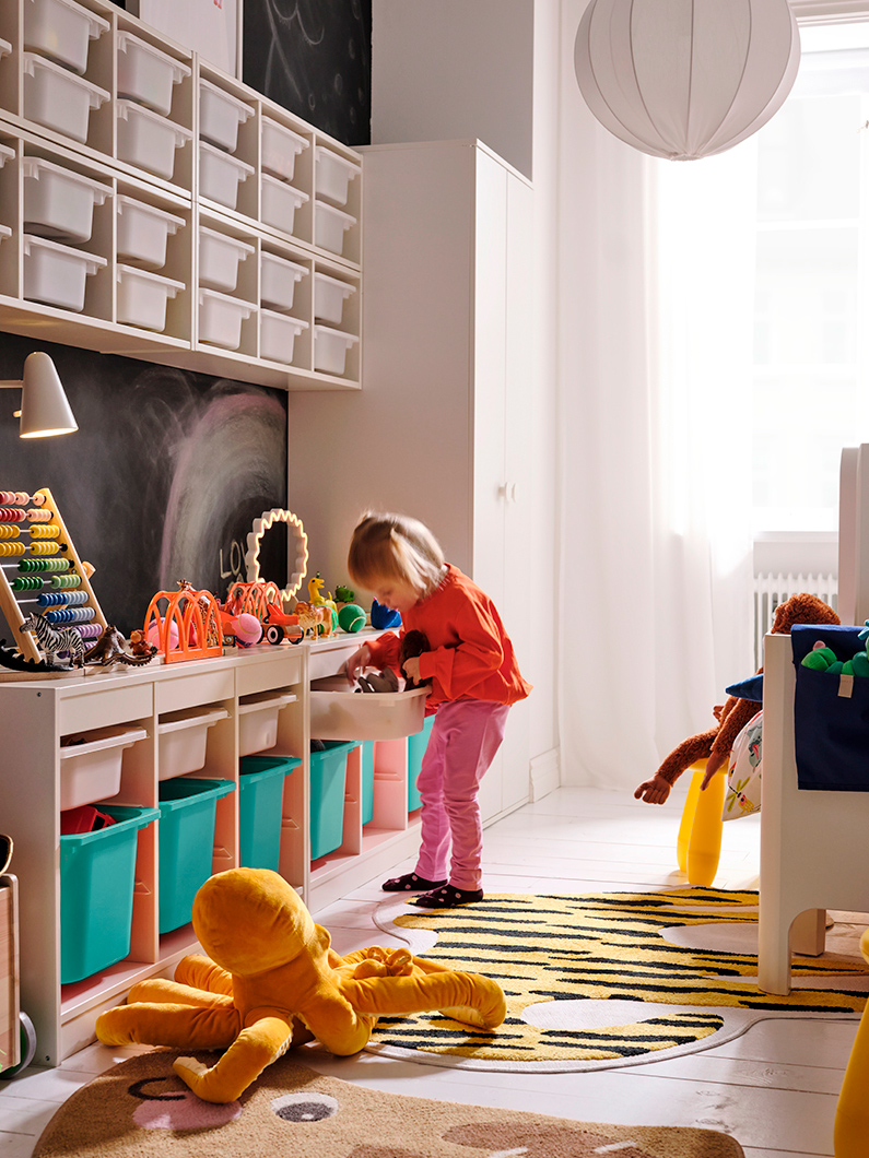 Una niña buscando juguetes dentro del sistema de almacenamiento TROFAST, y un pulpo de peluche BLÅVINGAD en el piso.