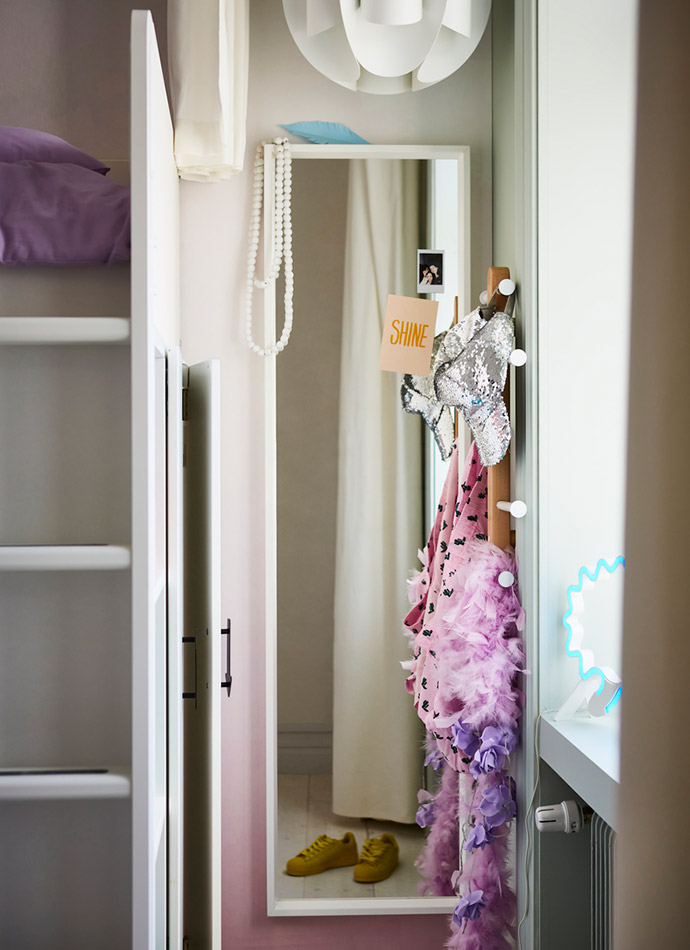 In the image, a full-length mirror with a white frame, a pink and yellow coat, pearls, and a blue light create a bright, youthful atmosphere.