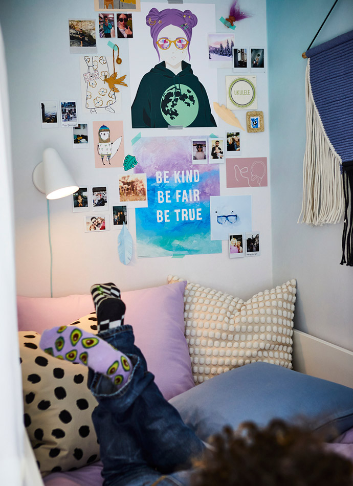 The image shows a wall with colorful posters and photos, purple and beige cushions, and fun socks. Youthful and personalized atmosphere.