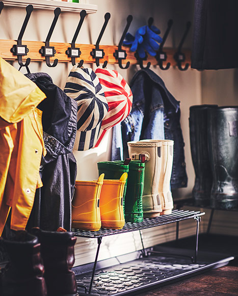 Metal shoe rack with yellow and green rain boots beneath a coat rack with coats and caps.