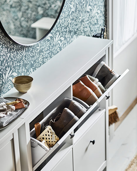 Narrow white shoe cabinet with tilt-out drawers and organized shoes in the hallway.