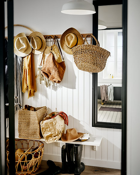 Hallway with straw hats and bags hanging on the wall, a mirror, and a bench.