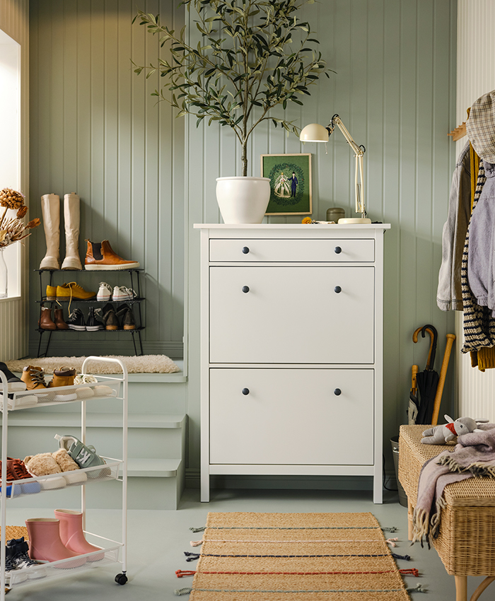 White shoe cabinet with tilt drawers, a plant, shoe shelves, and a rug in the entryway.