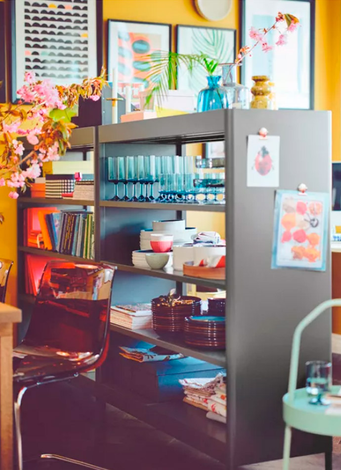 A dark shelving unit with blue glasses, plates, and books, in a vibrant setting with yellow walls.