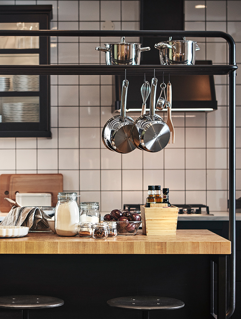 detail of a kitchen island with oak countertop, with various utensils on top and a rail with pans hanging on top.
