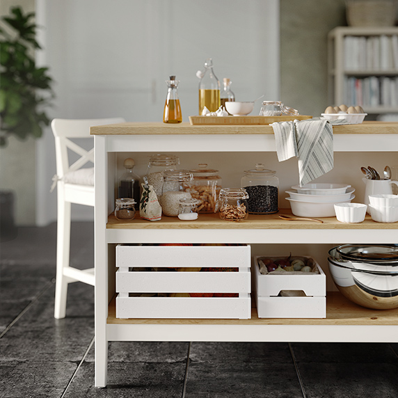 Detail of the lower part of a kitchen island with white base and pine worktop with wooden boxes and crockery in the lower part.