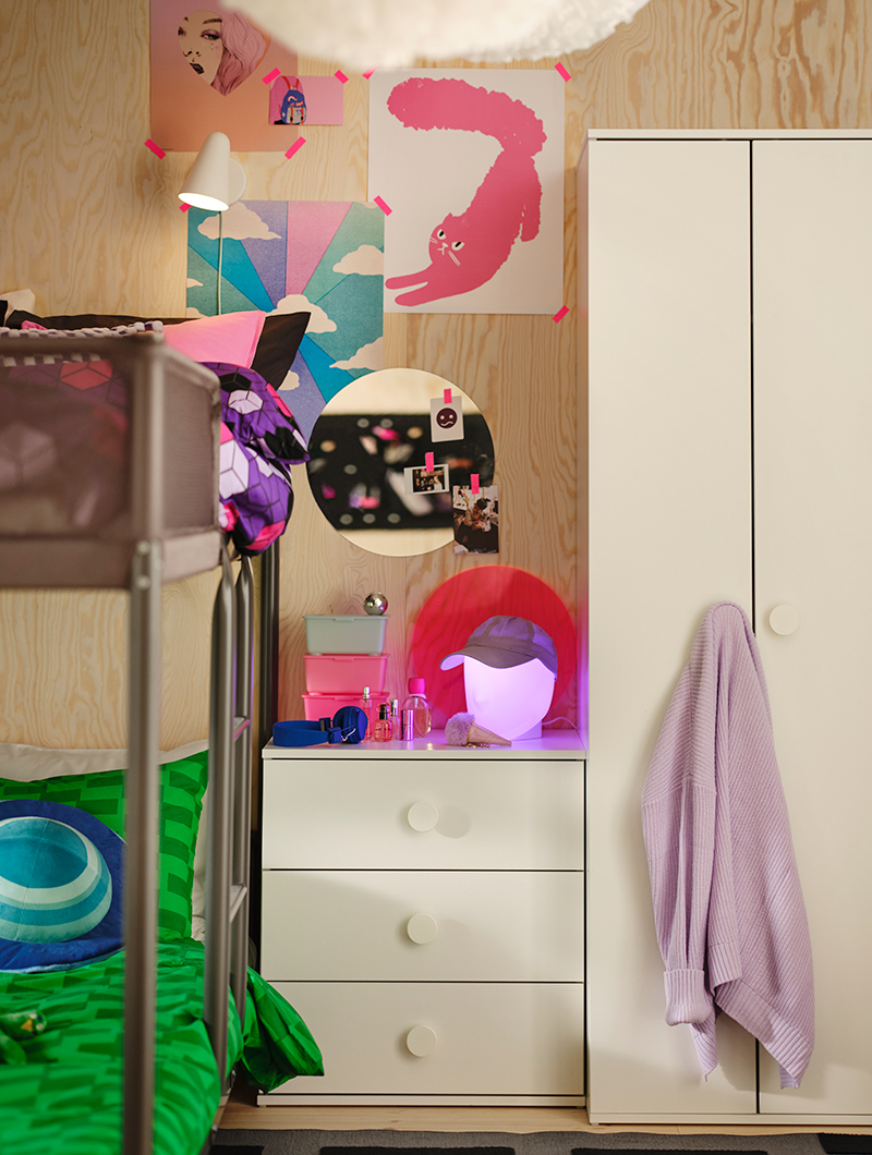 Youth bedroom with bunk beds, white dresser, and wardrobe. Vibrant posters and pink lights create a cheerful and personalized ambiance.