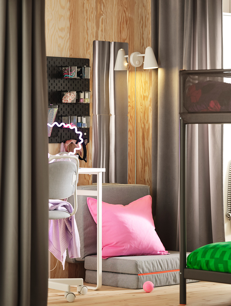 Youth bedroom with bunk beds, desk, and gray curtains. A vibrant pink cushion and neon light add a modern and playful touch.