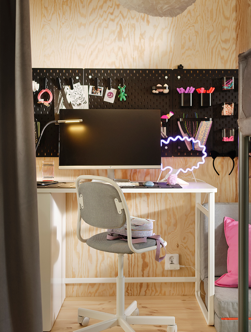 A white desk with a monitor, chair, and a black pegboard full of accessories. A modern and functional study ambiance in a youth room.