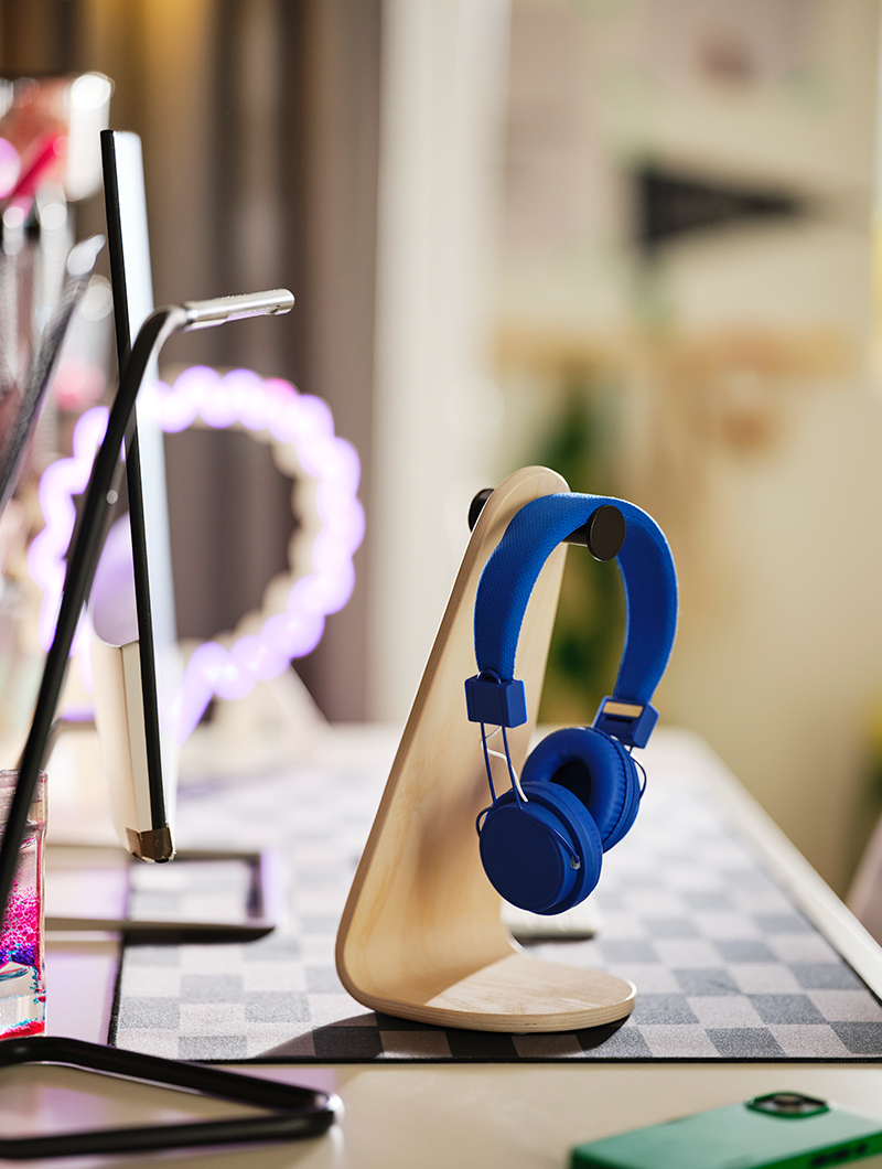Blue headphones on a wooden stand on a desk with a checkerboard mat. A youthful and organized study ambiance.