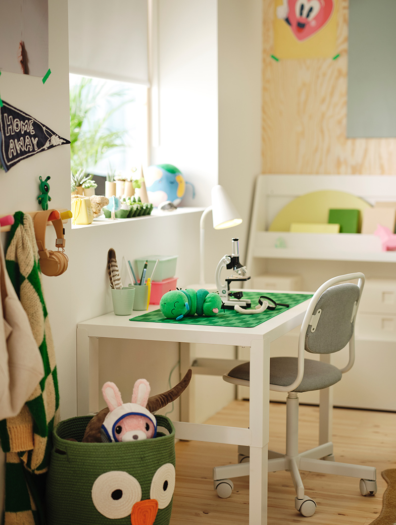 Children's bedroom with a white desk, gray chair, and a microscope on a green mat. Bright ambiance conducive to study and play.