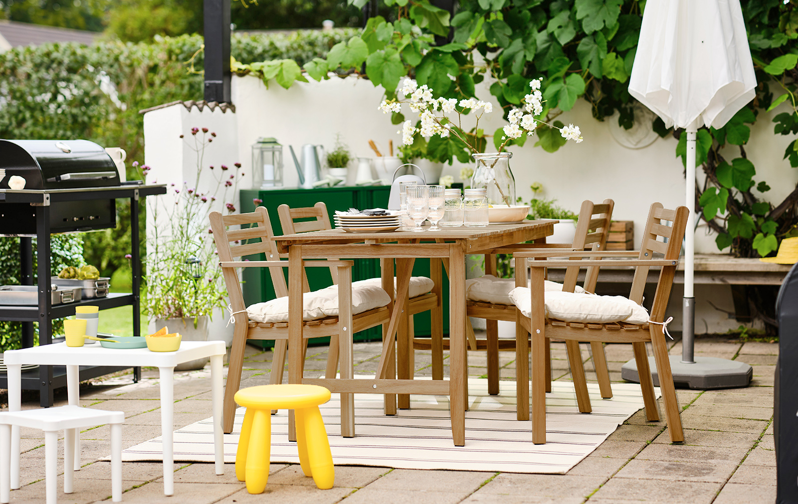 Barbecue area, with an outdoor table with 4 chairs, in front a small plastic dining area for children, in the background a barbecue and a closed parasol.