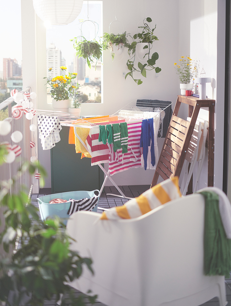 White outdoor armchair, on a balcony, there is a portable clothesline with colorful clothes hanging in the background.