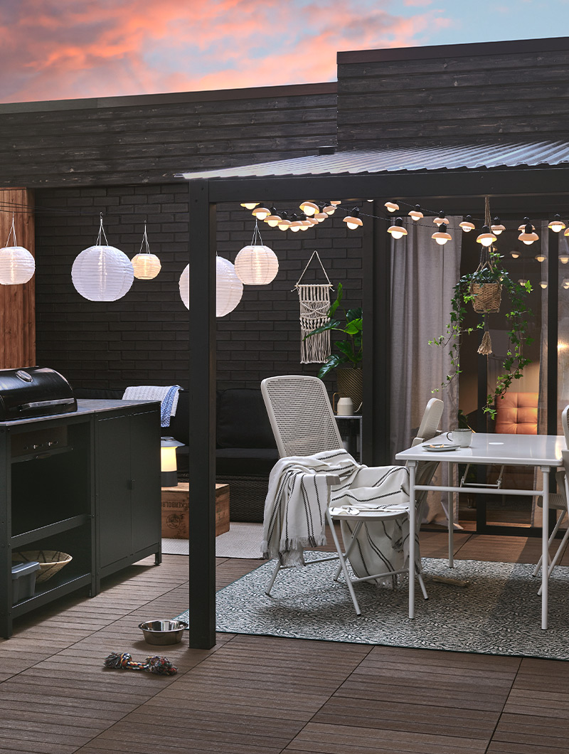 Patio oscuro con parrilla, comedor exterior y luces blancas colgantes. Crea un ambiente nocturno acogedor para reuniones al aire libre.