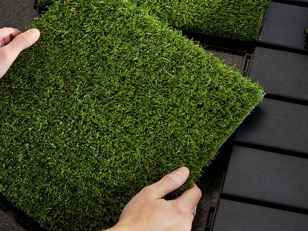 Artificial grass being placed on black surface by two hands